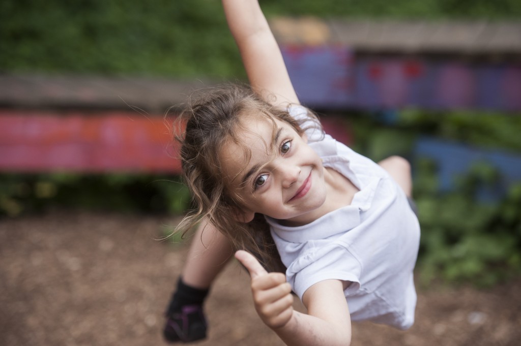 Girl swings and gives thumbs up sign in adventure playground