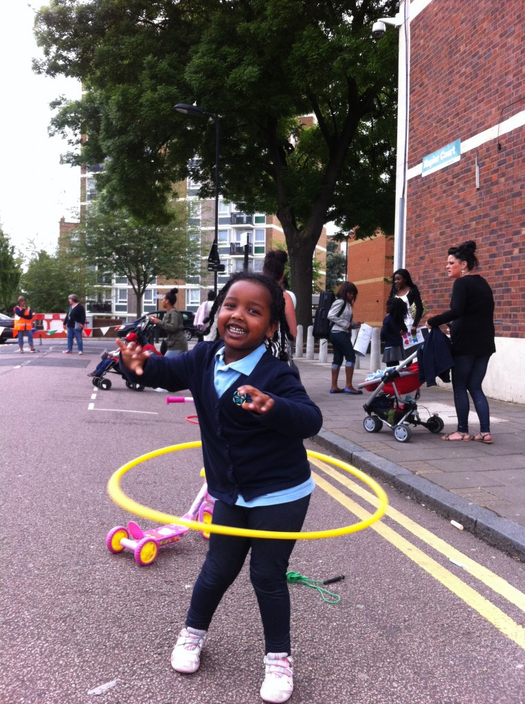 Smiling girl hula hoops in street during playing out session outside a school